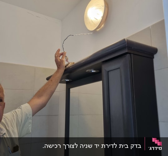 אדם מחזיק חוט חשמל ליד מנורה על הקיר